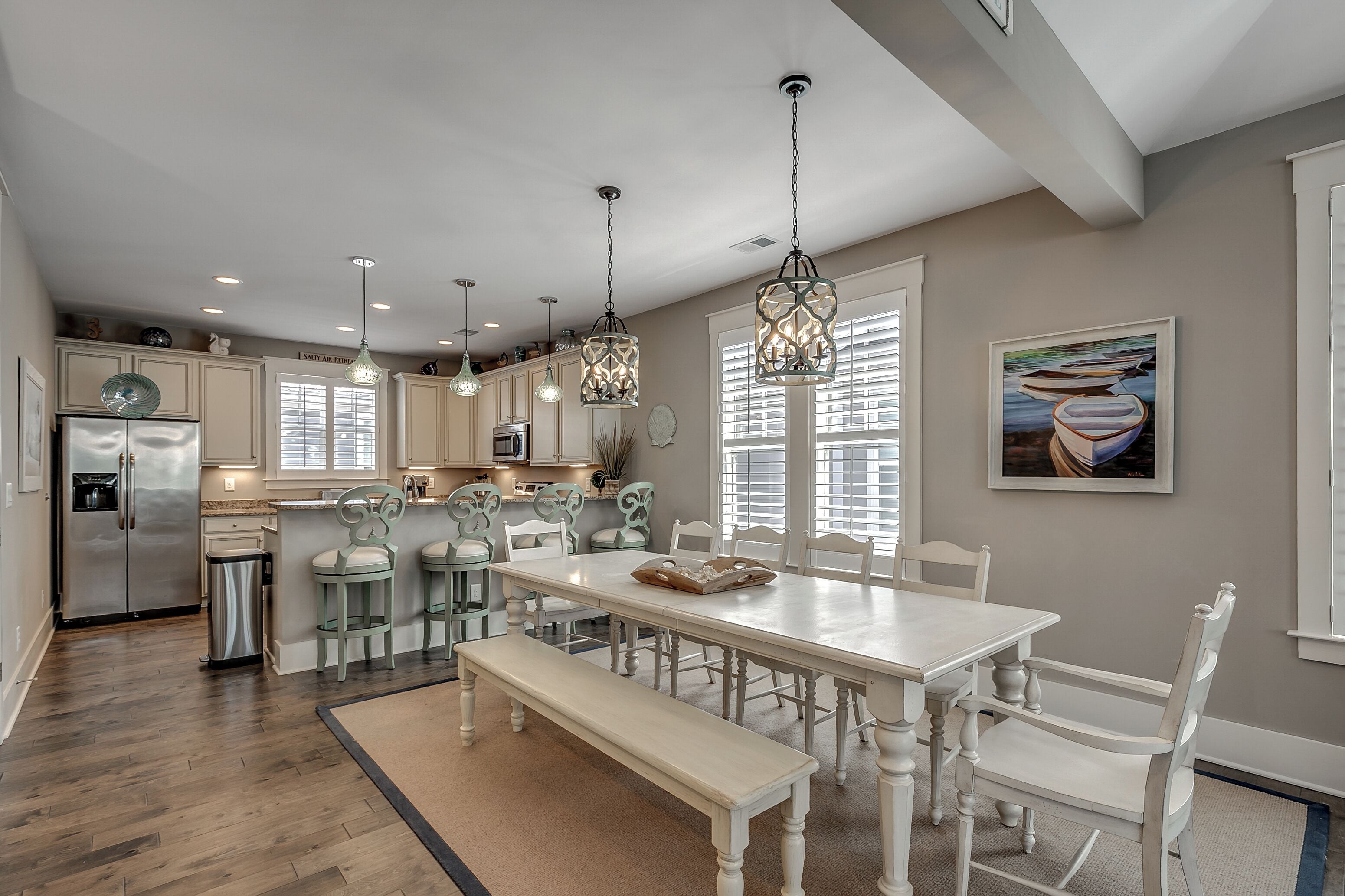 A spacious kitchen with a large island, pendant lights, and a dining area with white chairs and a bench.
