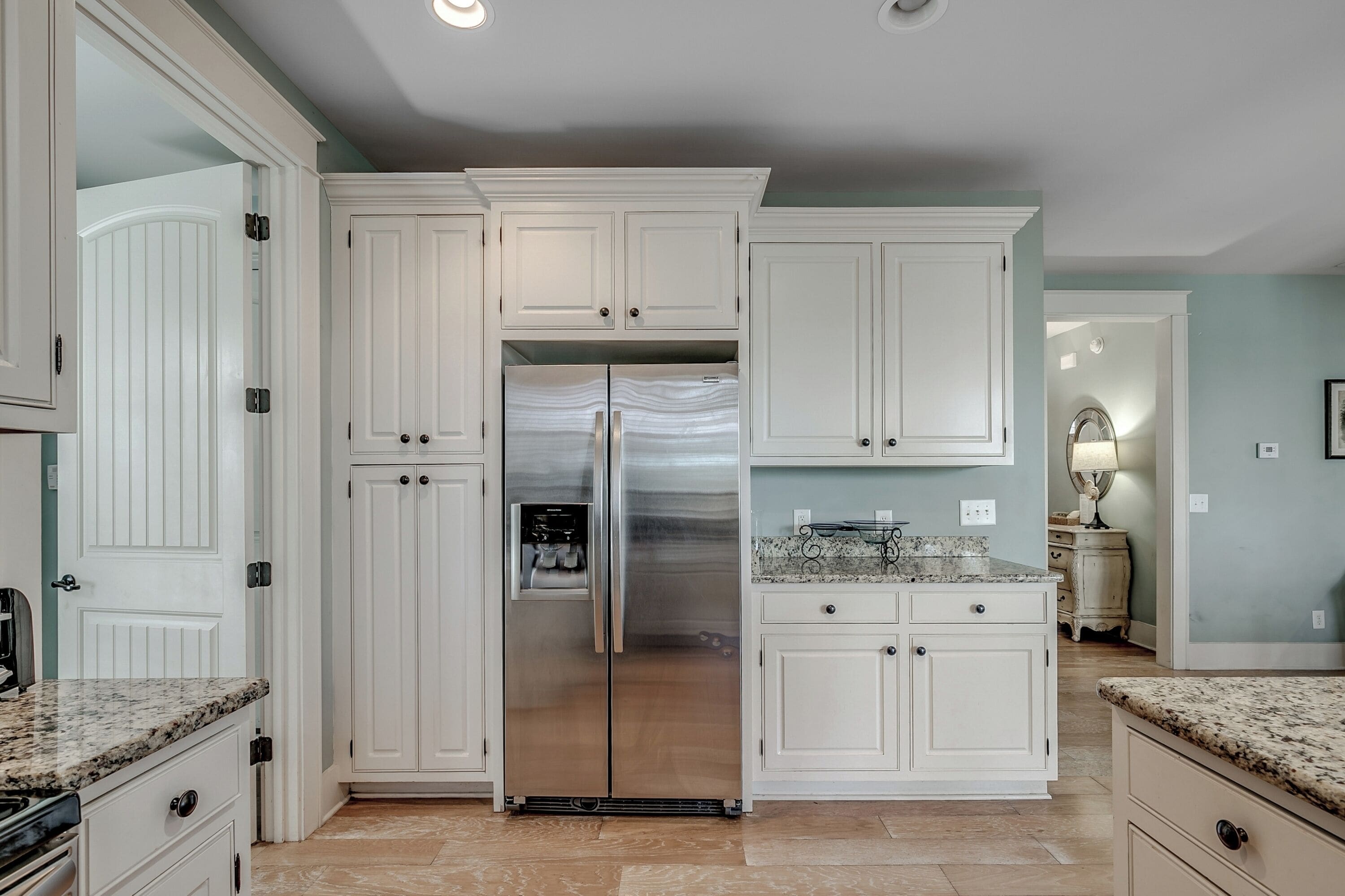 A kitchen with white cabinetry, a stainless steel refrigerator, granite countertops, and a tiled floor.