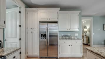 Una cocina con armarios blancos, un refrigerador de acero inoxidable, encimeras de granito y piso de baldosas.