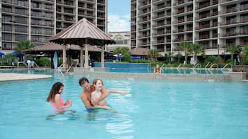 Relax by the pool surrounded by lounge chairs and umbrellas under a shaded pavilion.