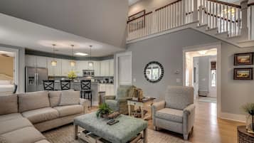 A spacious living room with a high ceiling, a staircase leading to an upper level, and a kitchen in the background.
