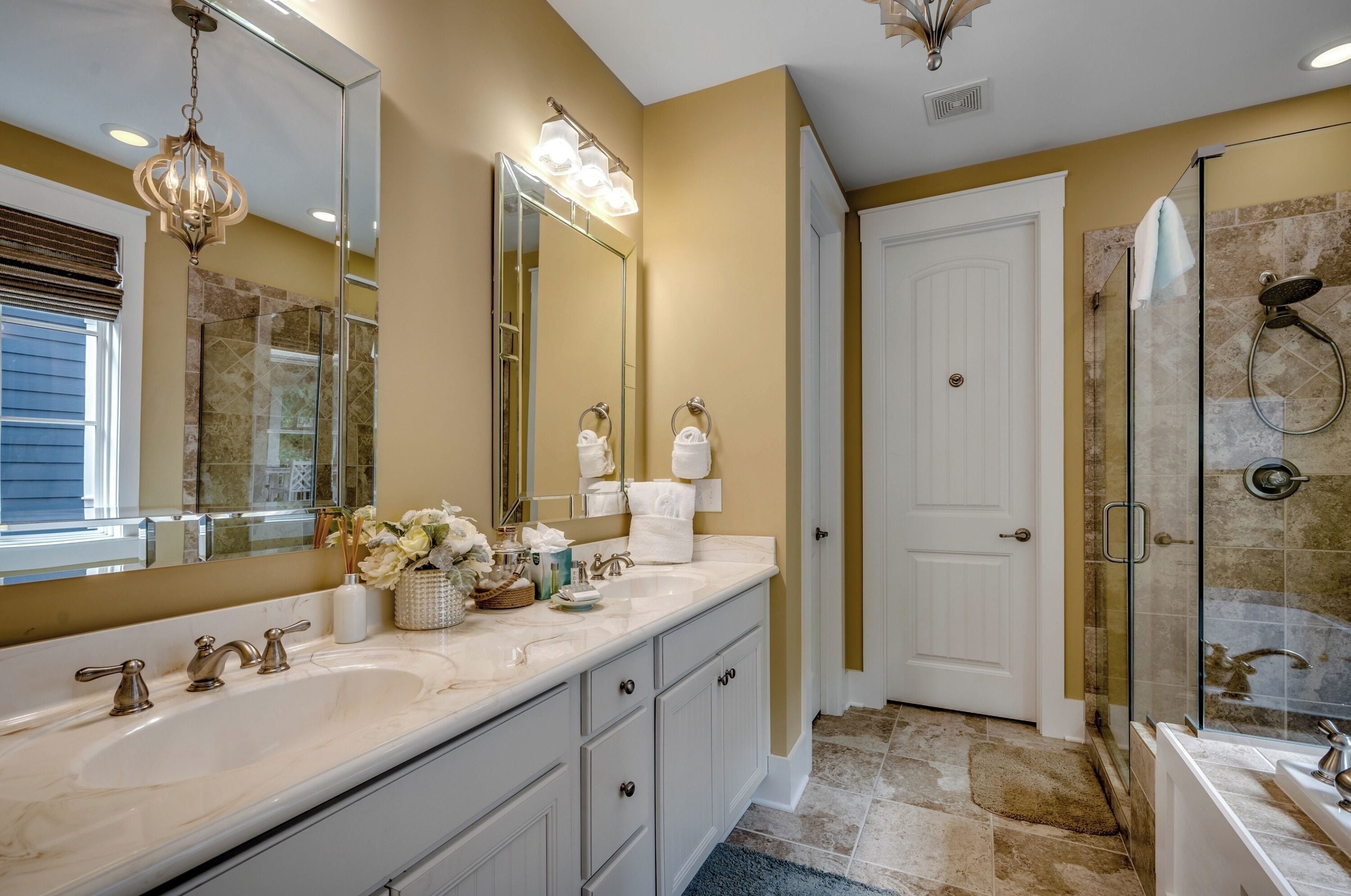 Une salle de bain avec un double vasque, un grand miroir, un lustre et une cabine de douche en verre.