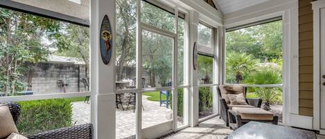 A sunroom with large windows, wicker furniture, and a view of a garden.