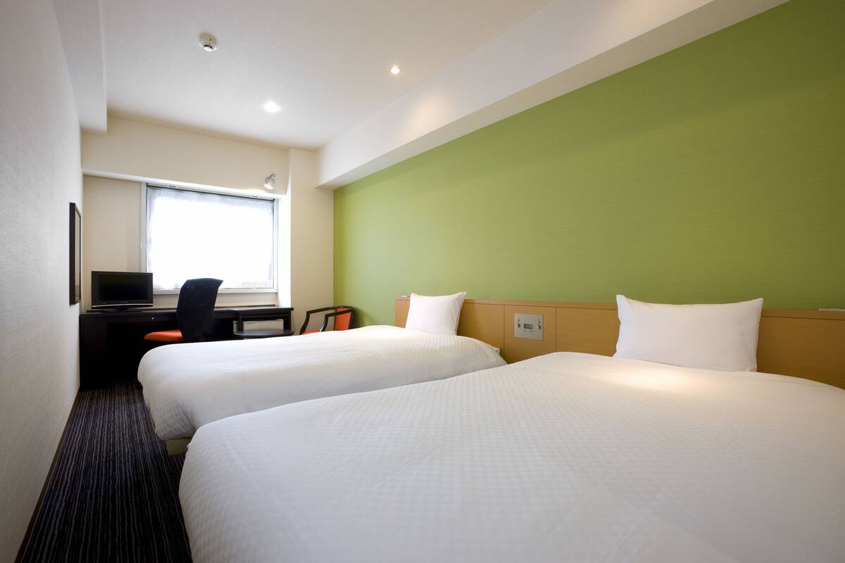 Une chambre d’hôtel avec deux lits, un bureau, une chaise et une fenêtre.