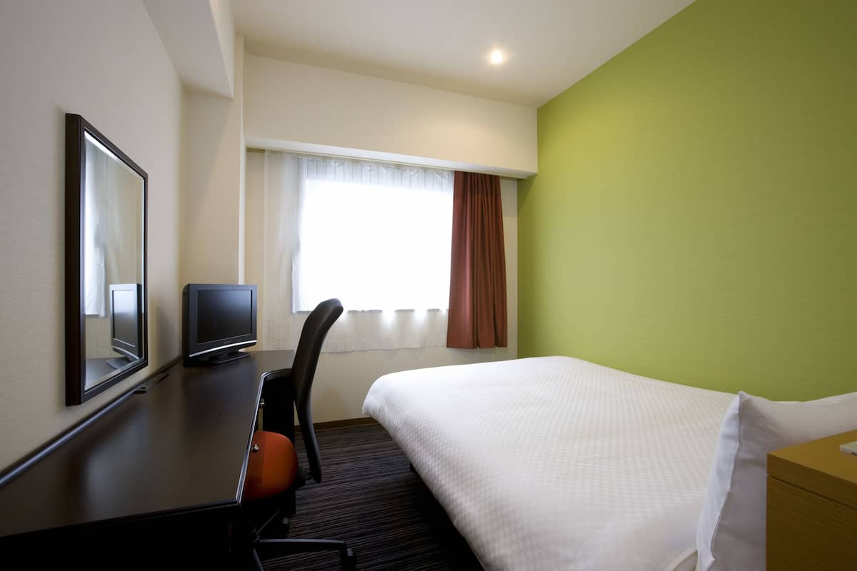 Une chambre d’hôtel avec un lit, un bureau et une chaise, une télévision et une fenêtre avec des rideaux.