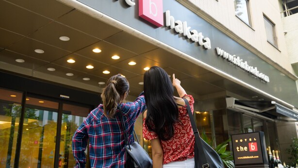 Entrada de un hotel con un cartel que dice "the b hakata" y una dirección web.