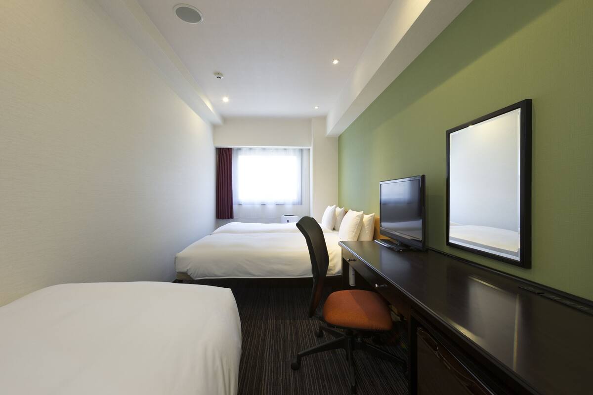 Une chambre d’hôtel avec deux lits, un bureau avec une télévision et une grande fenêtre avec des rideaux.