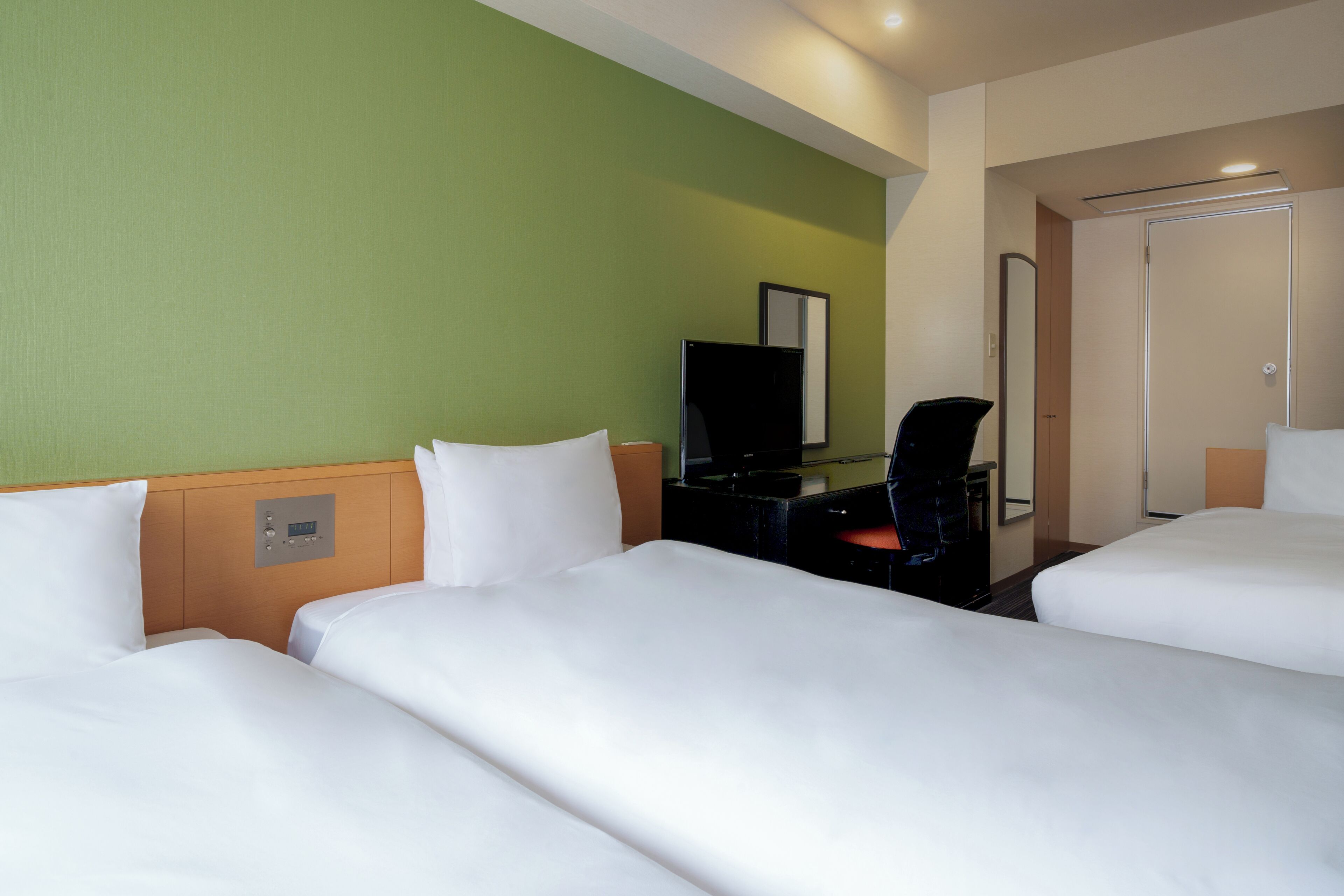 Una habitación de hotel con tres camas, un escritorio, un televisor y un armario.