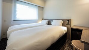 Habitación de hotel con dos camas, un ventanal grande y un escritorio empotrado con silla.