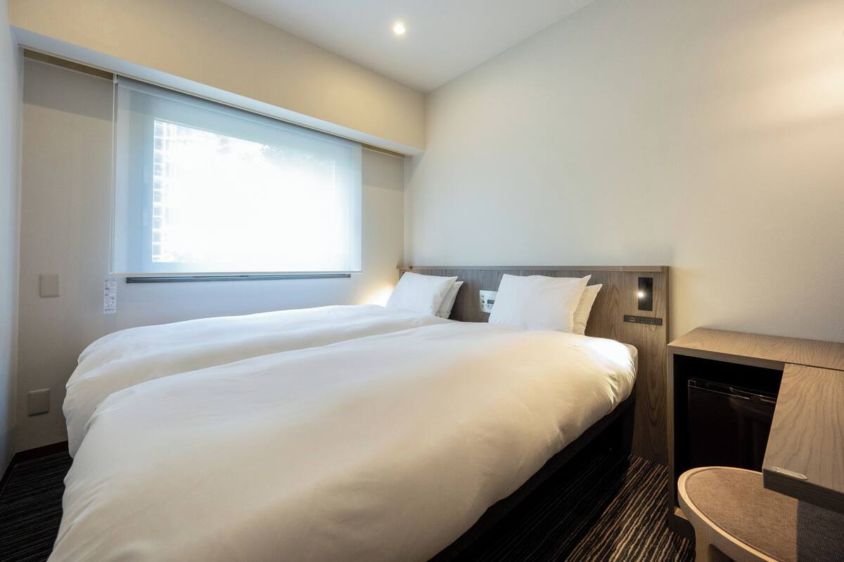 Une chambre d’hôtel avec deux lits, une grande fenêtre et un bureau intégré avec une chaise.