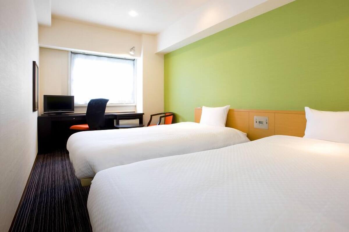 Une chambre d’hôtel avec deux lits, un bureau avec une chaise, une télévision et une fenêtre.