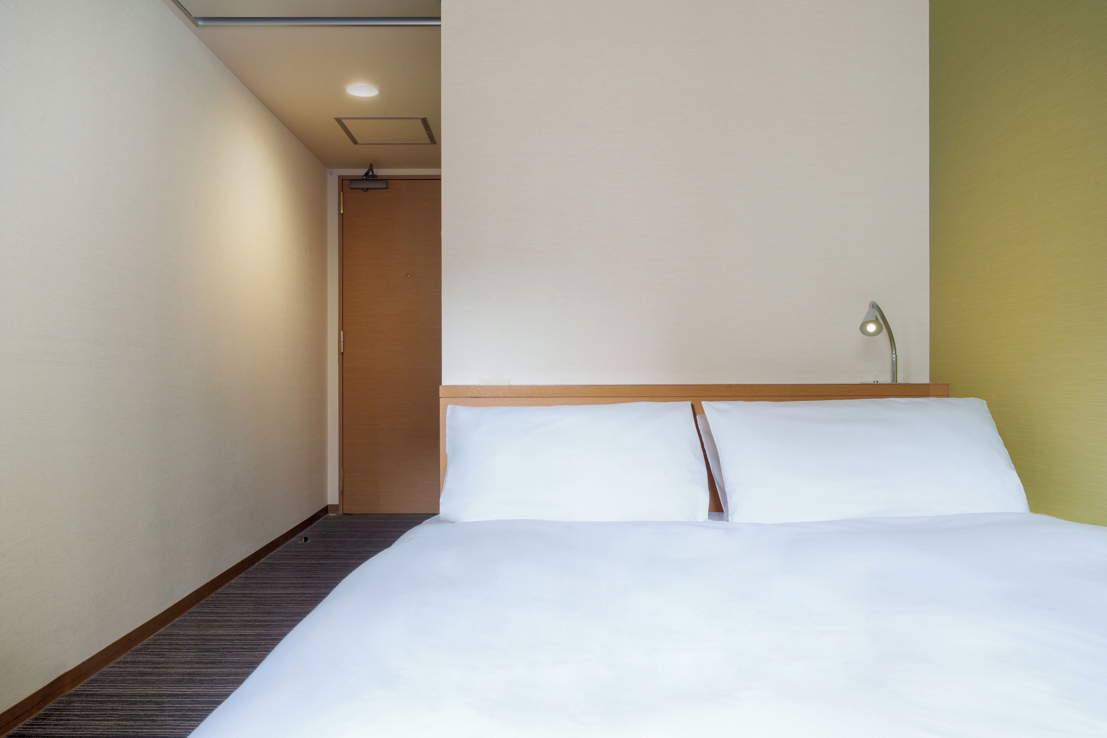 Una habitación de hotel con una cama, una mesita de noche, una lámpara y una puerta que da a otra habitación.