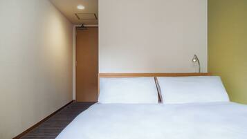 Una habitación de hotel con una cama, una mesita de noche, una lámpara y una puerta que da a otra habitación.