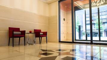 Un vestíbulo con dos sillones rojos, una mesita y un puerta de cristal que da al exterior.