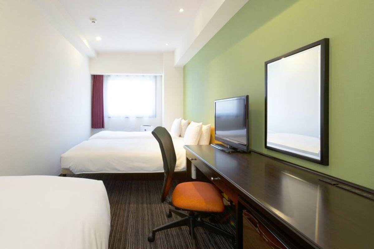 Une chambre d’hôtel avec deux lits, un bureau avec une télévision et une grande fenêtre avec des rideaux.