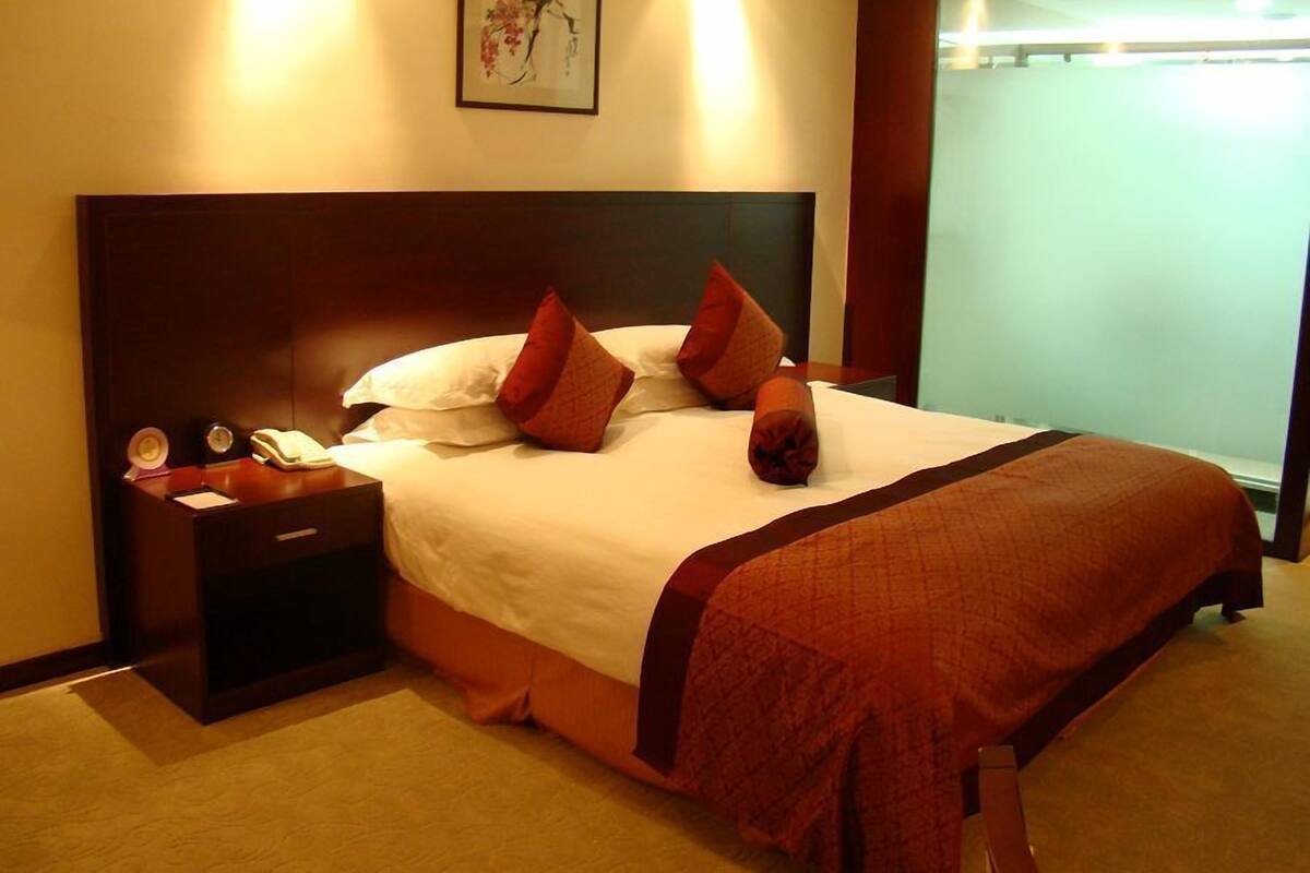Habitación de hotel con una cama grande, una mesita de noche con teléfono y bloc de notas, un cuadro en la pared y una ventana con cortinas.
