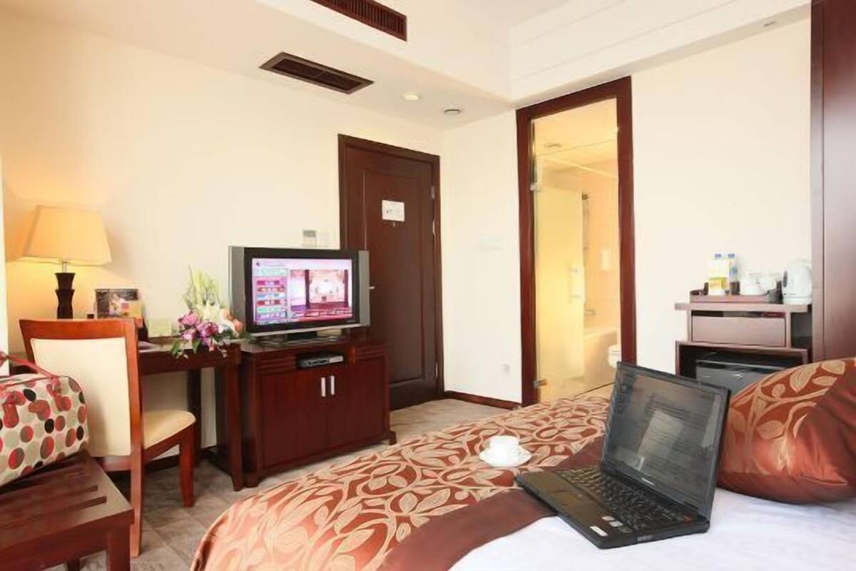 Una habitación de hotel con una cama, un escritorio con televisor, una computadora portátil y una silla.