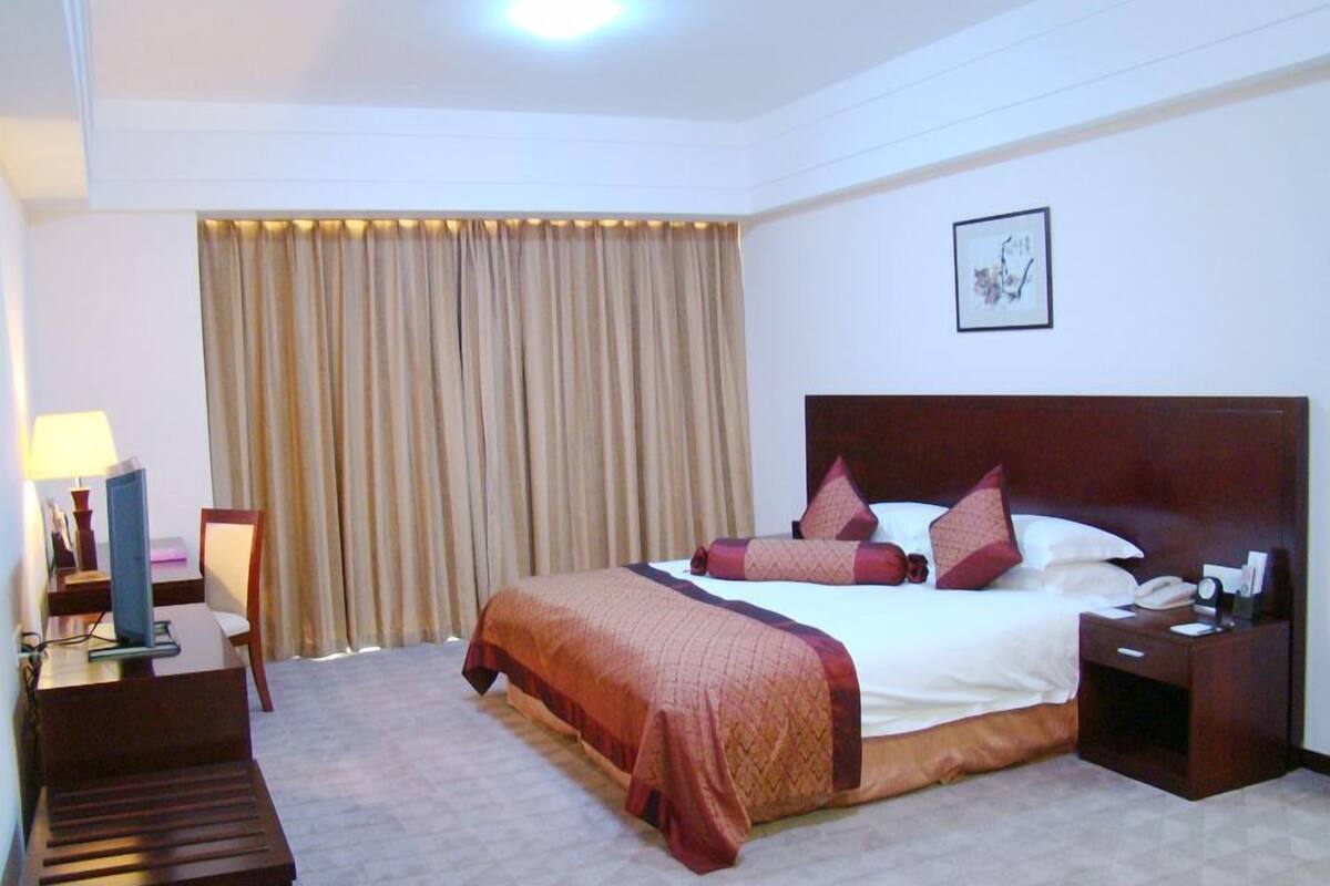 Una habitación de hotel con una cama grande, un escritorio, una silla y una mesita de noche con teléfono y lámpara.
