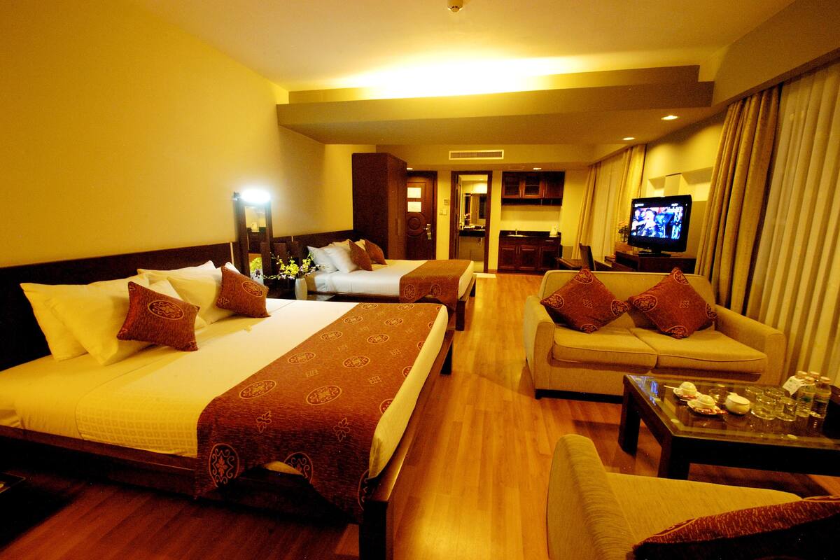 A hotel room with two beds, a sofa, a TV, and a small table with items on it.