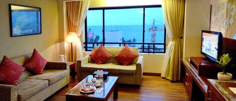 Una sala de estar con un sofá, una mesa de centro, un televisor y un ventanal con vistas al mar y una grúa.