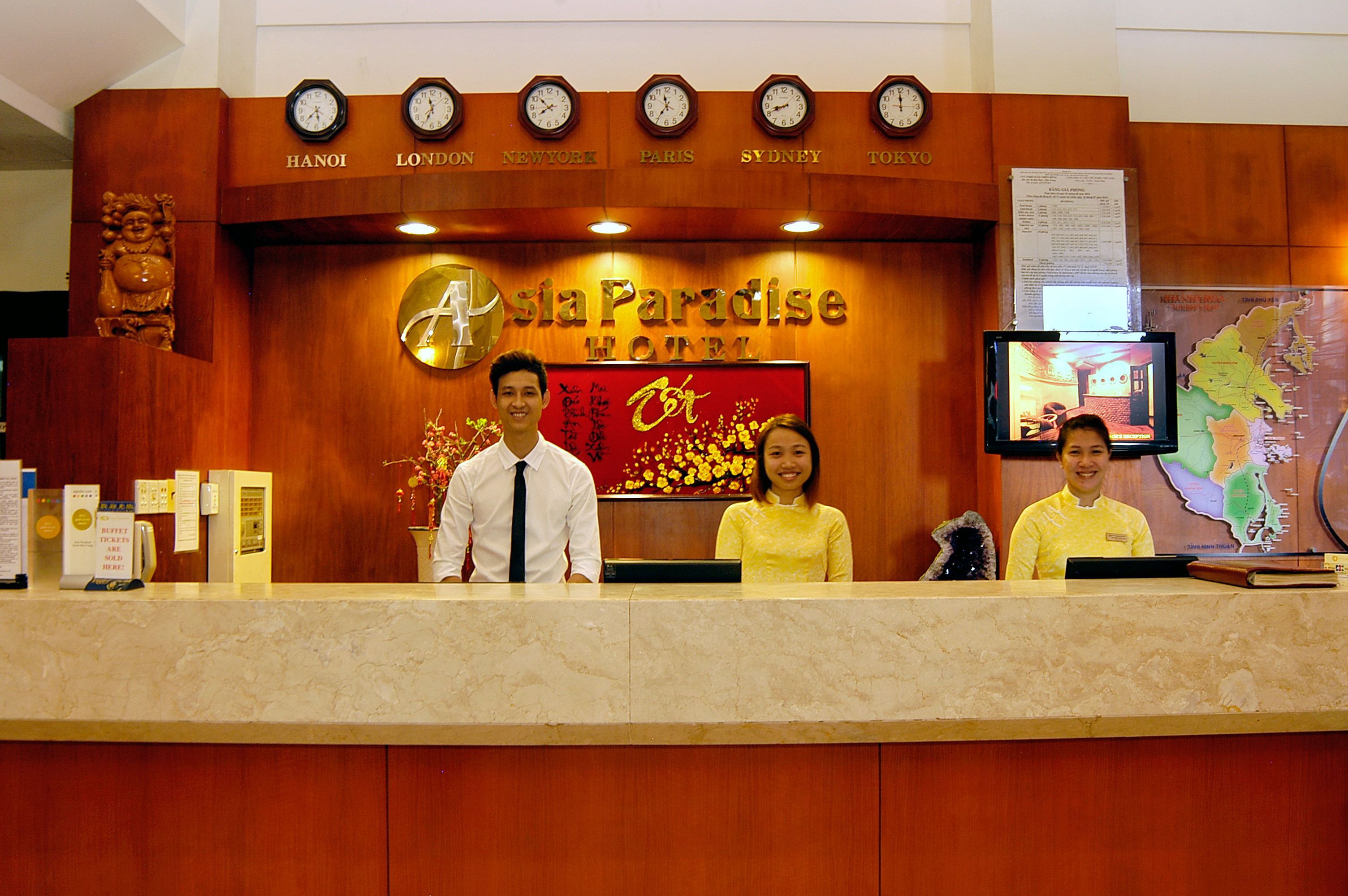 A reception desk at the Asia Paradise Hotel with clocks displaying different city names and a map on the wall.