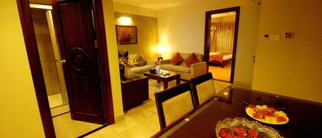 A hotel room with a dining table, chairs, a sofa, a coffee table, and a small dining table with plates of food.