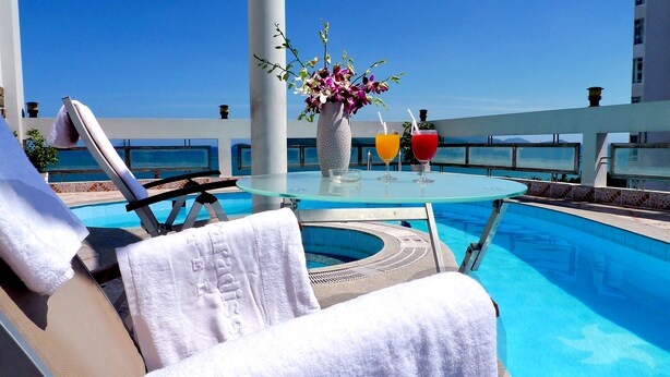 A poolside area with a glass table, a vase of flowers, and two drinks. - Asia Paradise Hotel (Nha Trang)