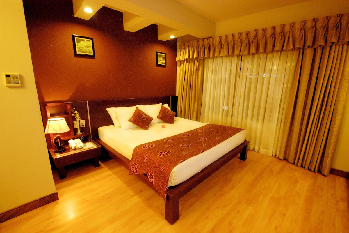 A hotel room with a large bed, a bedside table with a lamp, and curtains on the window.
