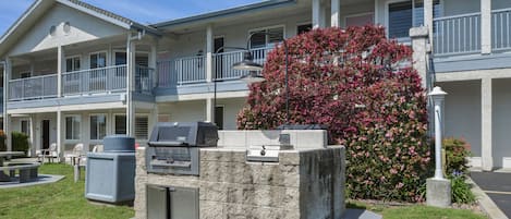 Un motel de dos pisos con un patio que incluye una parrilla y mobiliario exterior.