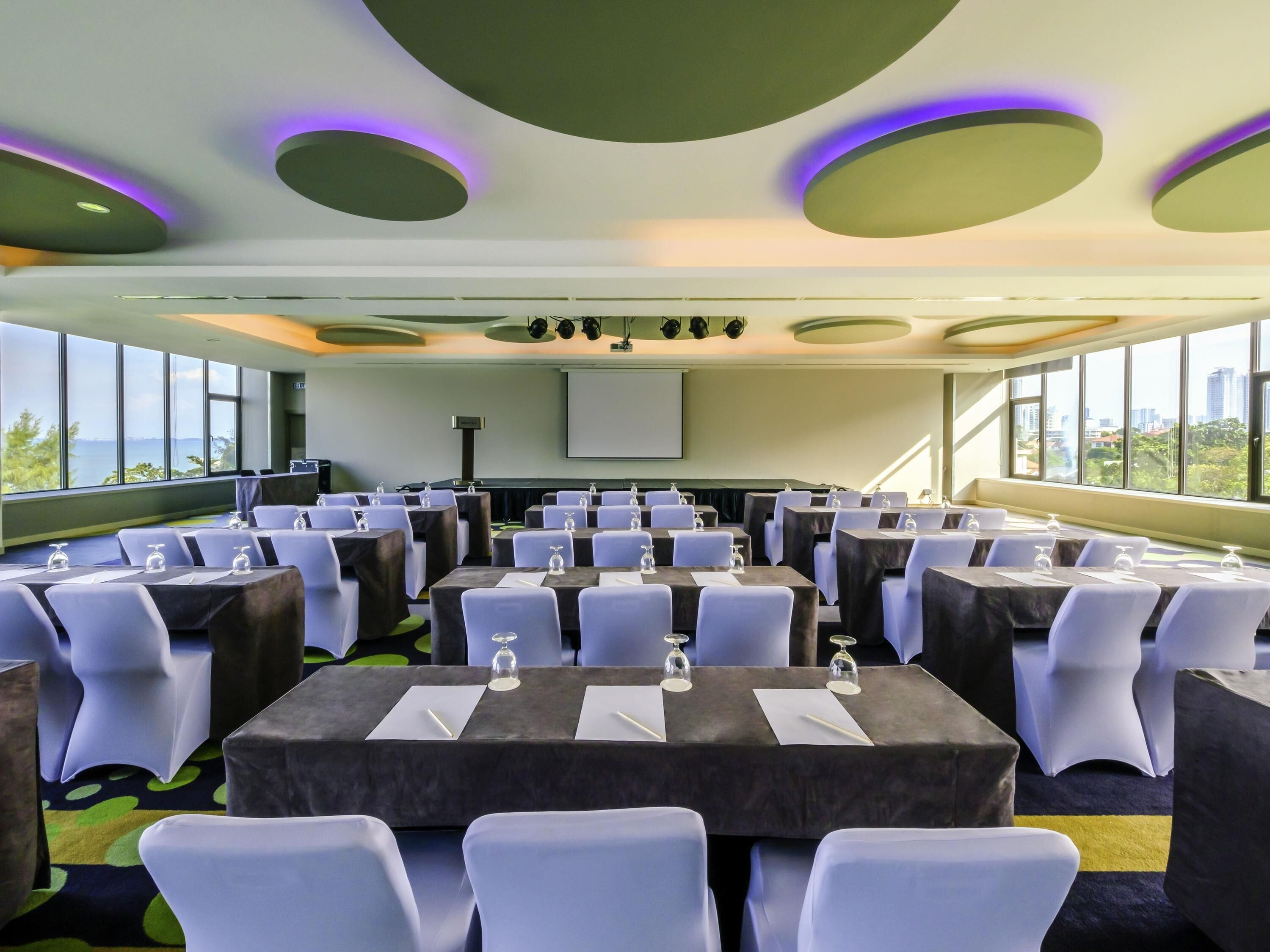 A conference room with tables, chairs, and a projector screen.