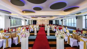 A banquet hall with tables set for a formal event, a red carpet, and a view of the sea through large windows.