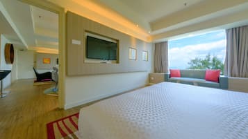Ein Hotelzimmer mit einem großen Bett, einem an der Wand montierten Fernseher, einer Couch mit Kissen und Blick ins Freie.
