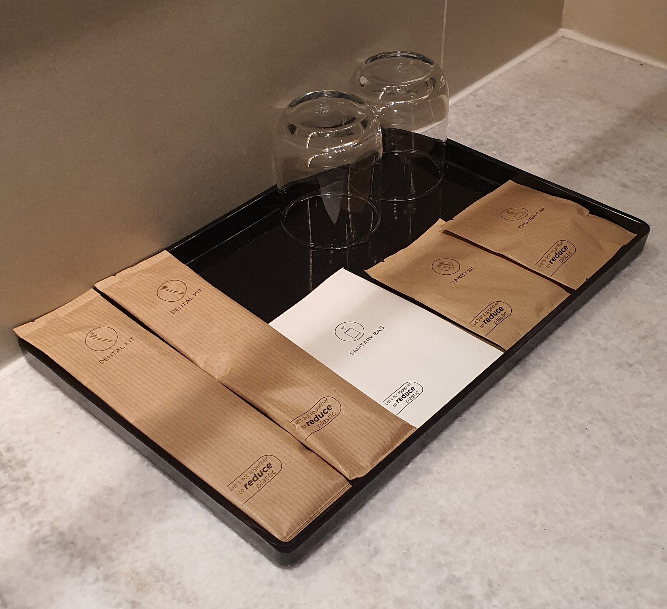 A tray with a dental kit, a sanitary bag, and a shower cap on a marble countertop.
