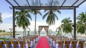 An outdoor wedding aisle with white chairs and a red carpet, palm trees, and a view of the ocean. - Mercure Penang Beach (George Town)
