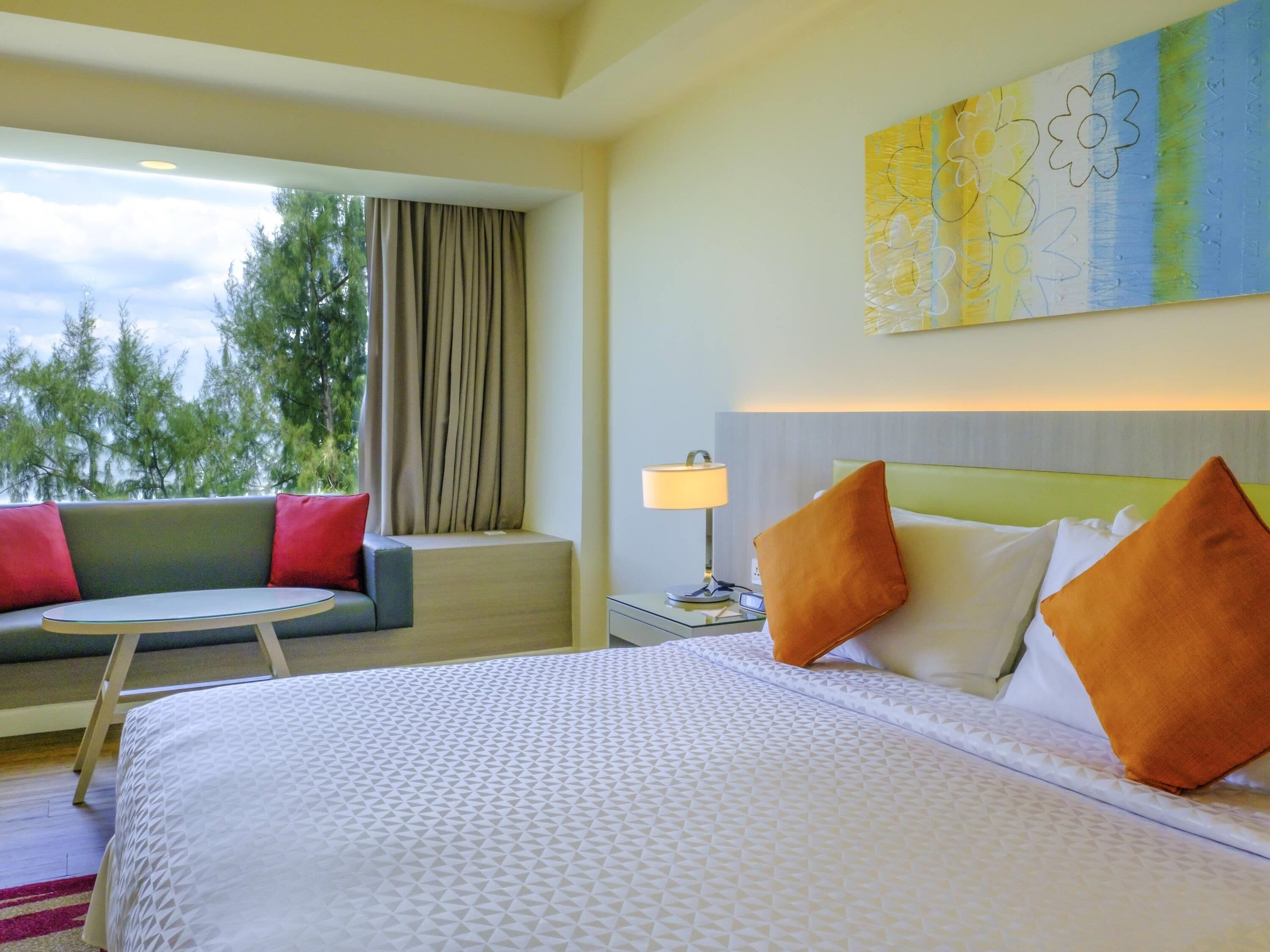 A hotel room with a bed, a sofa, a lamp, and a painting on the wall.