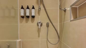 Ducha con cabezal de ducha manual y grifo empotrado. Hay tres botellas de champú y acondicionador en la pared.