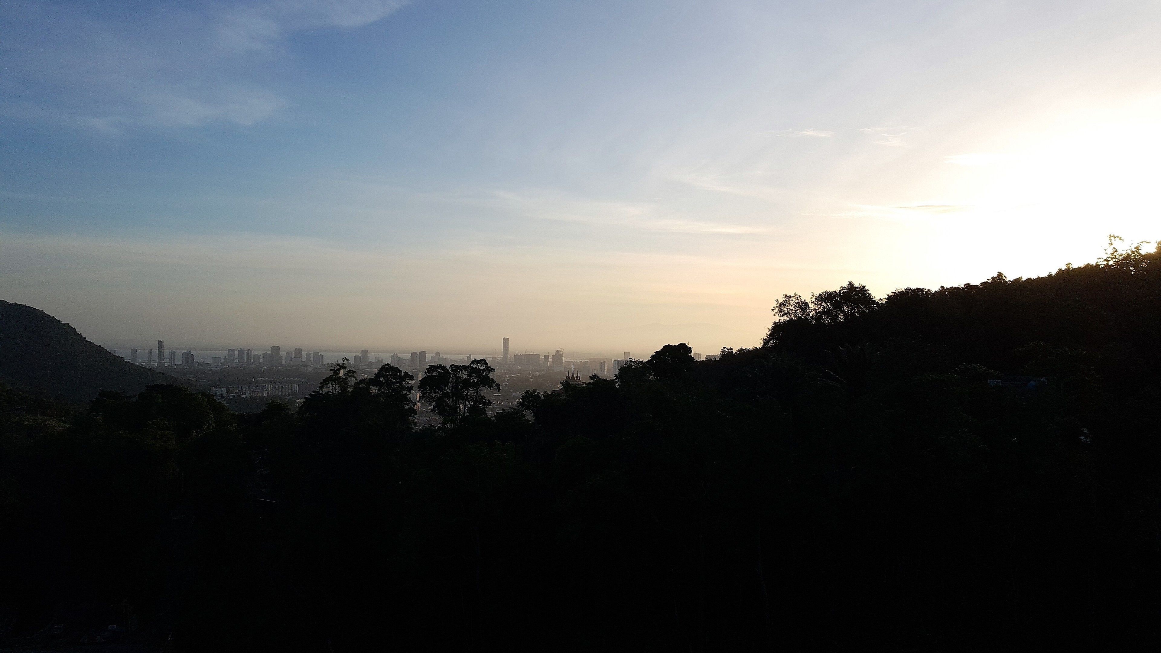 Une vue urbaine avec, au loin, des bâtiments et, au premier plan, une colline.