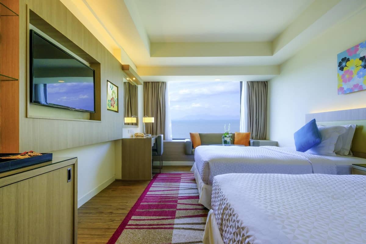 Ein Hotelzimmer mit zwei Betten, einem Schreibtisch, einem Fernseher und Meerblick.
