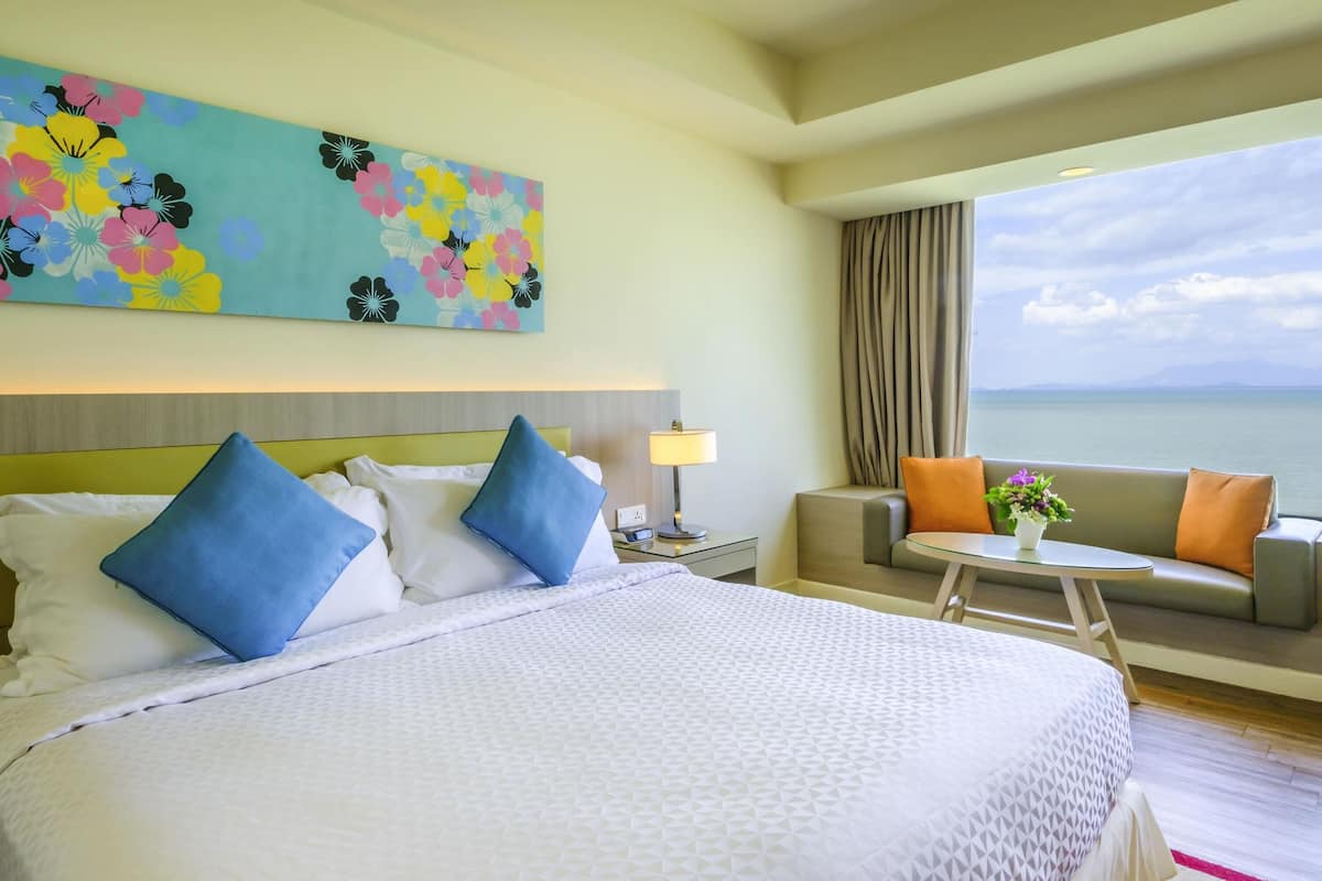 A hotel room with a large bed, a sofa, a small table, a lamp, and a painting on the wall.