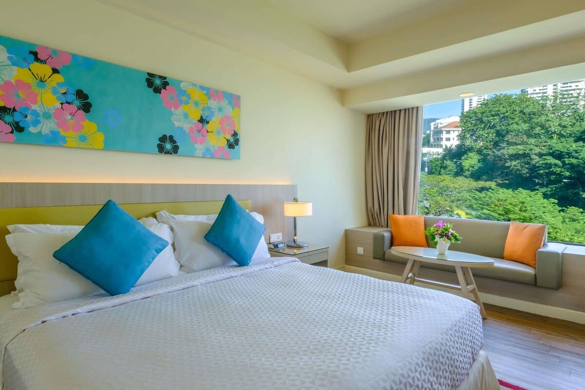 A hotel room with a large bed, a sofa, a small table, and a painting on the wall.
