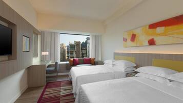 Habitación de hotel con dos camas, televisión, escritorio y ventana grande con vistas a edificios.