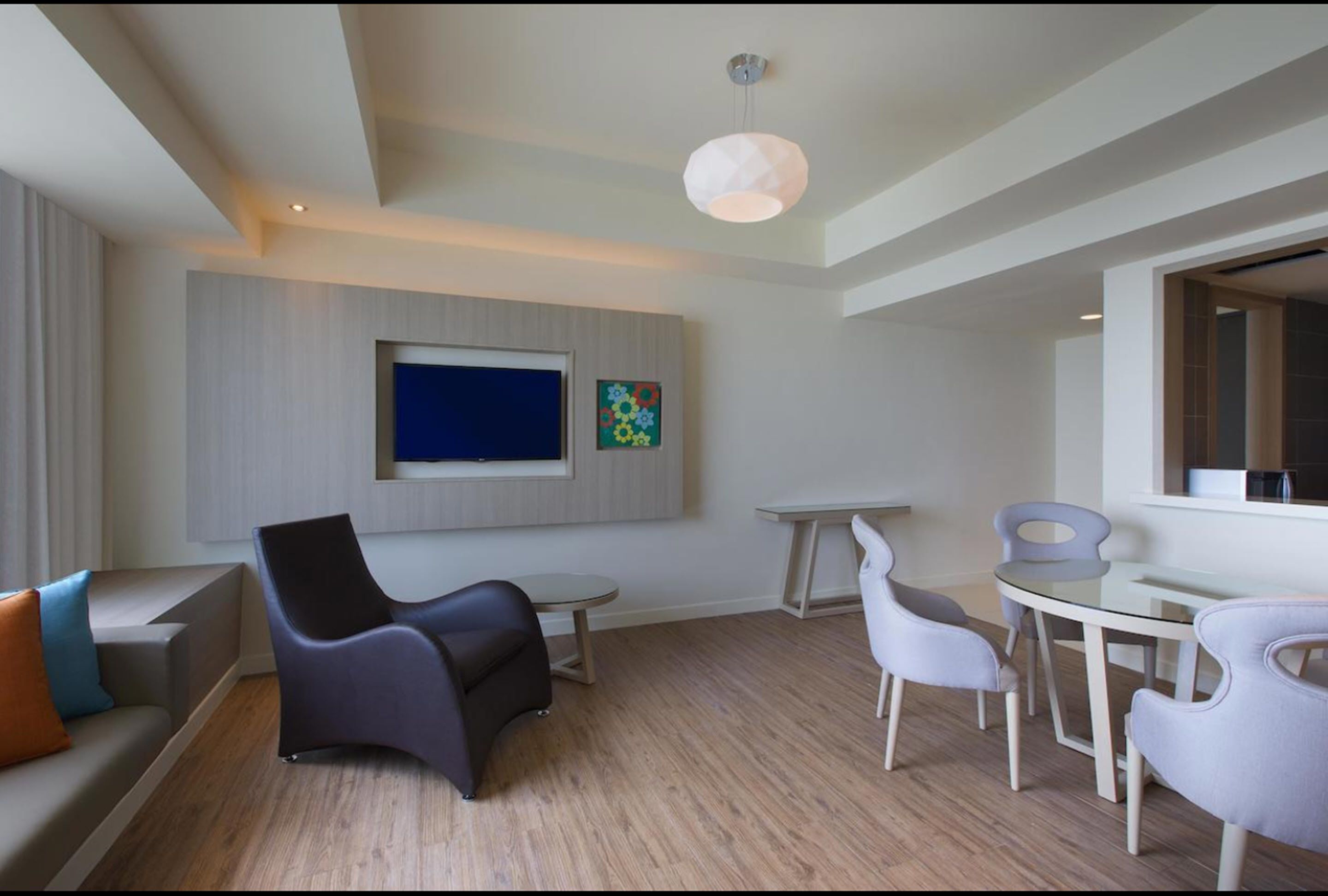 A modern living room with a flat-screen TV mounted on the wall, a round glass table, and contemporary furniture.