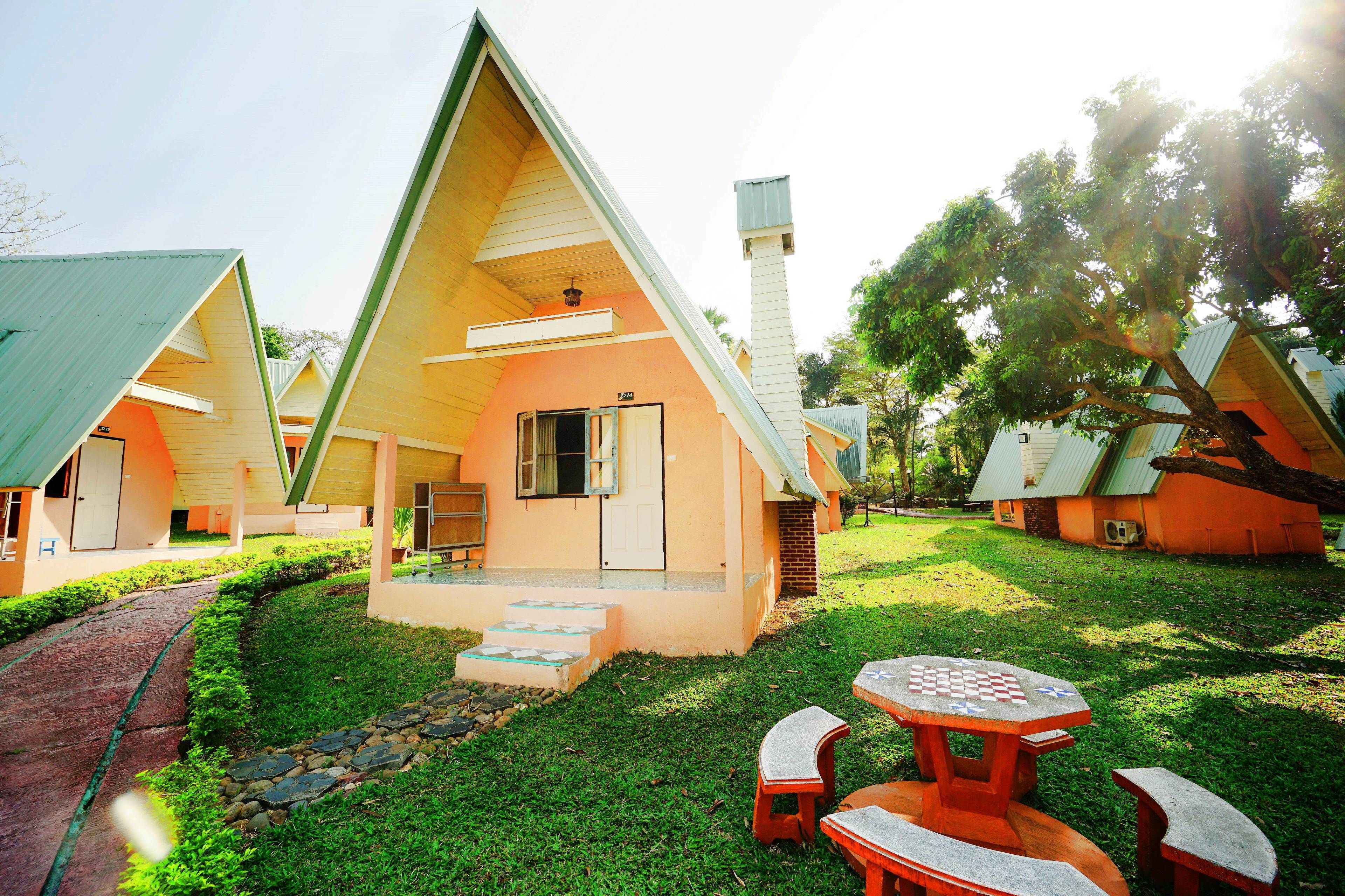 A row of triangular-roofed cottages with a paved path leading to a central picnic table.