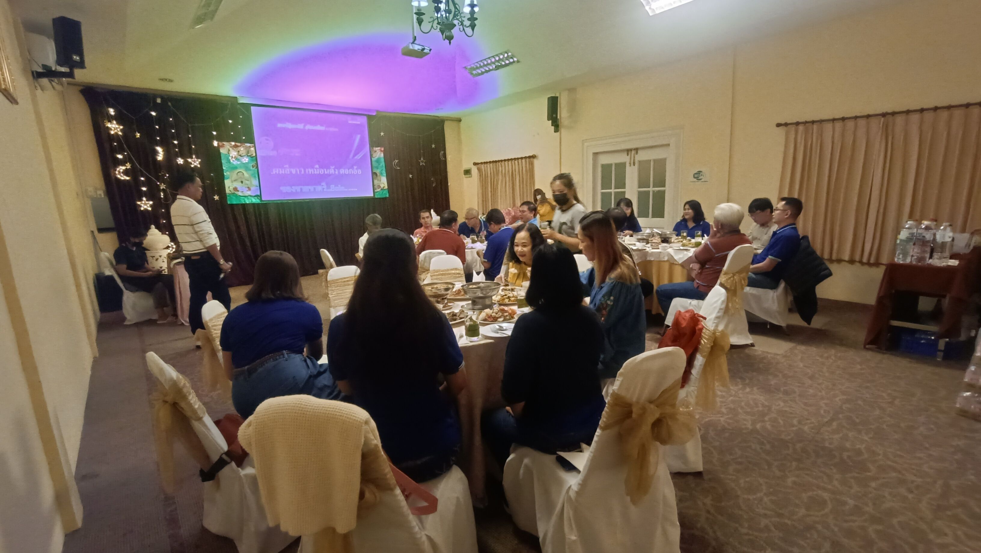 A conference room with round tables, attendees seated, and a presentation screen at the front.