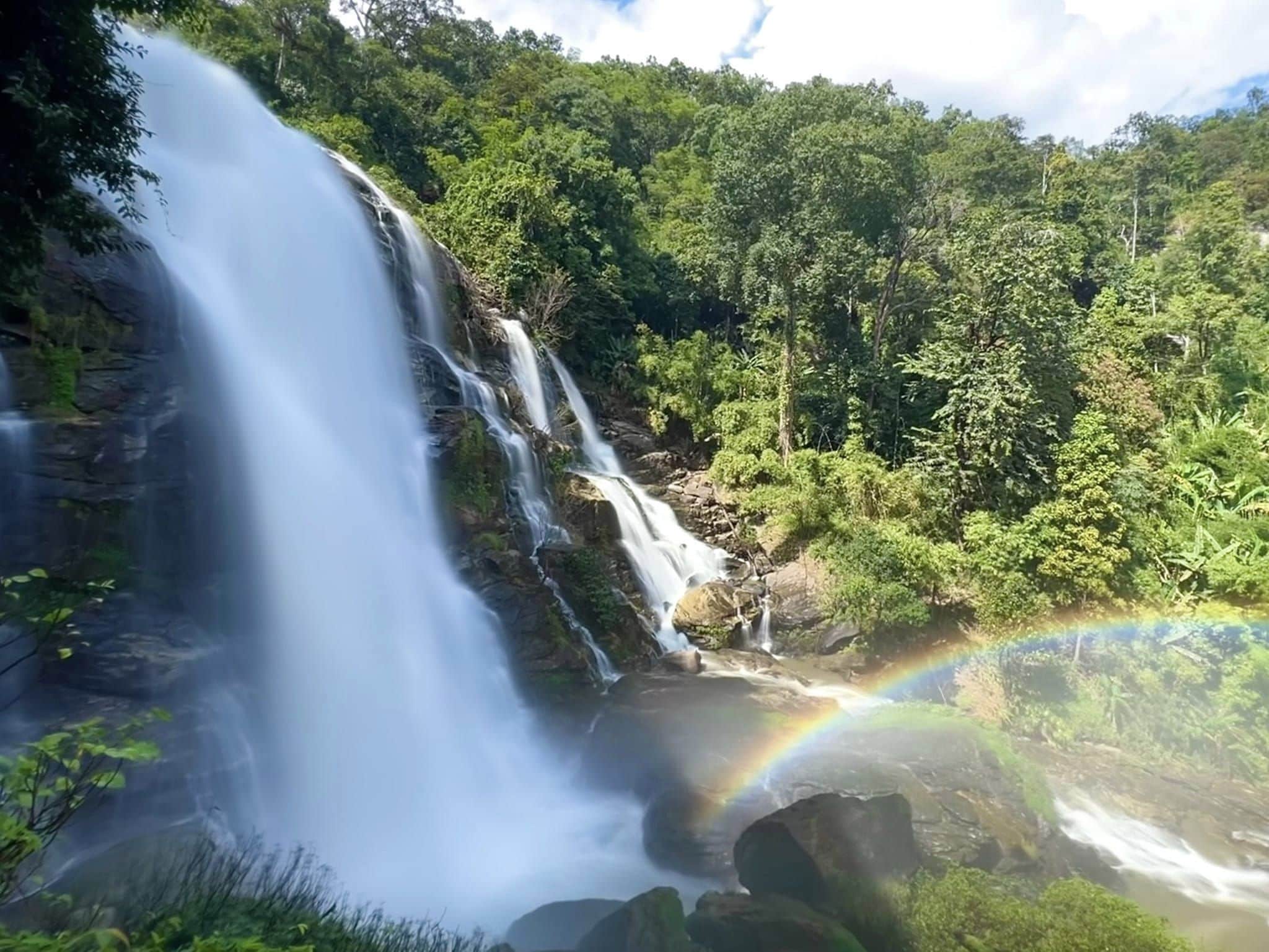 Een waterval stort over rotsen, omgeven door weelderige begroeiing.