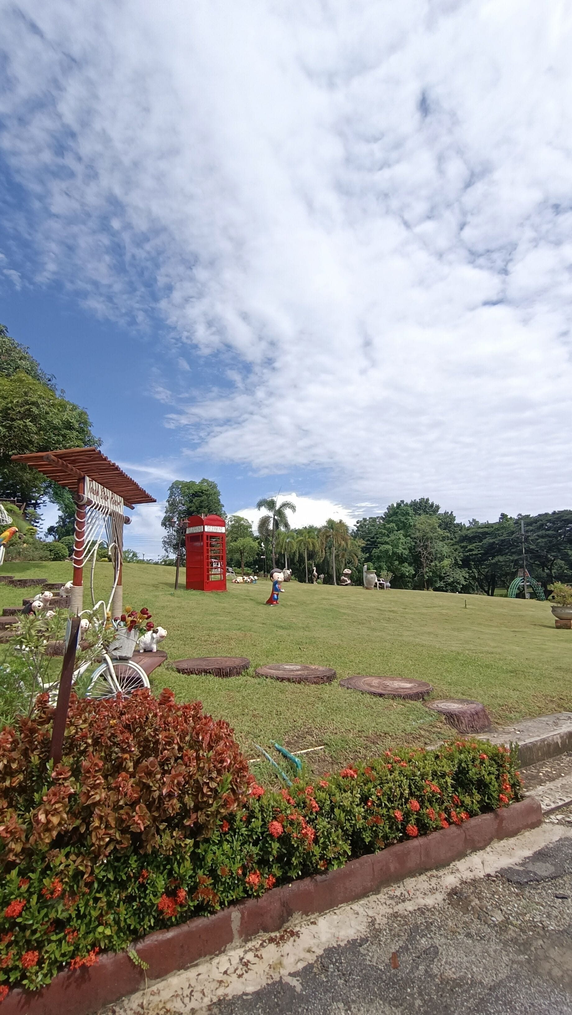 A park with a red telephone booth, a pergola, and a bicycle.