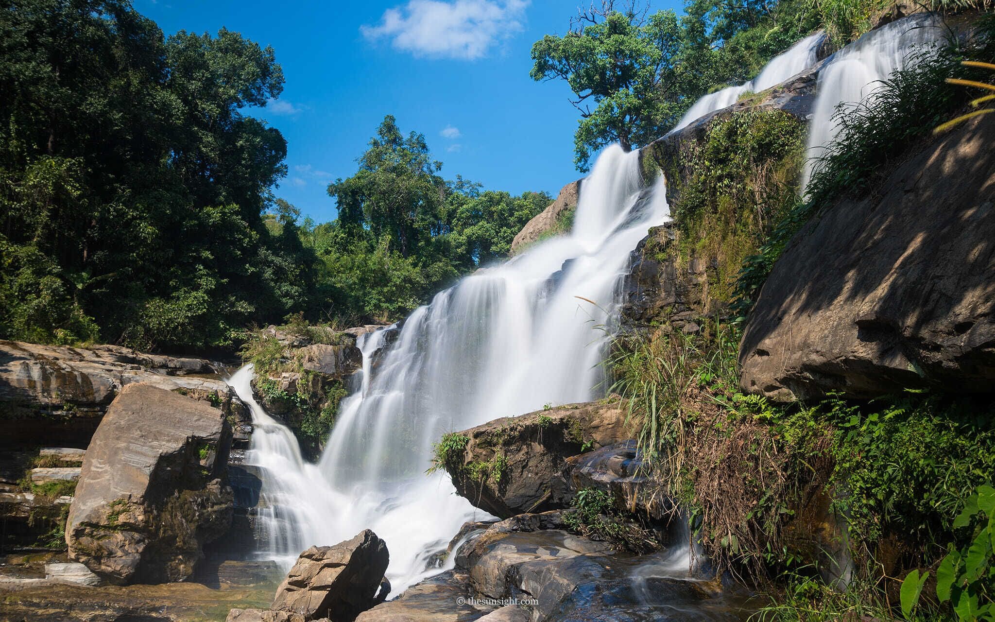 A waterfall cascading over rocks surrounded by lush greenery.