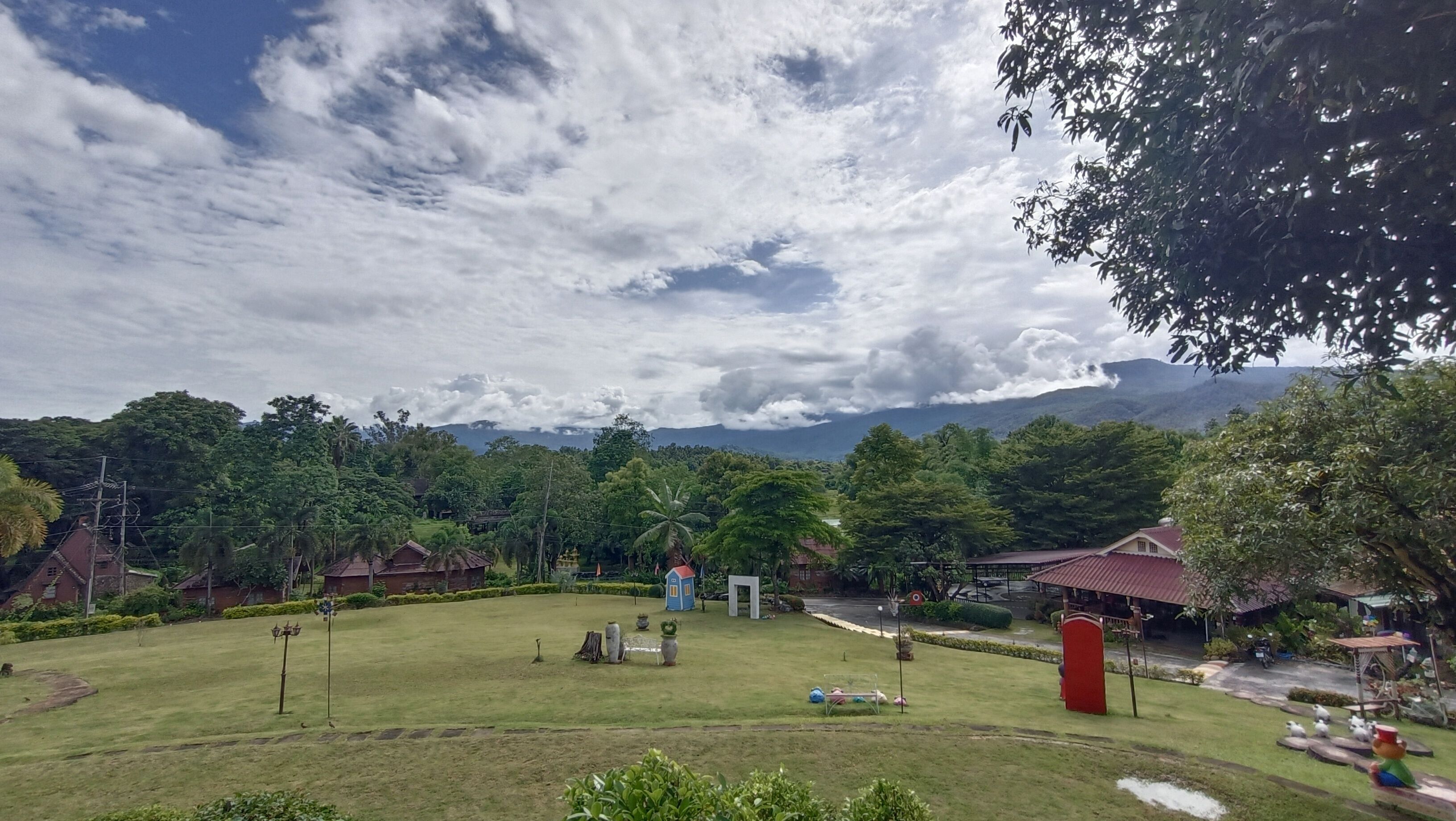 Un paisaje verde y exuberante con cielo despejado, un pequeño estanque y algunos edificios al fondo.