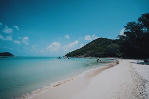 A beach with clear turquoise water, a sandy shore, and boats. - Havana Beach Resort (Ko Pha-ngan)