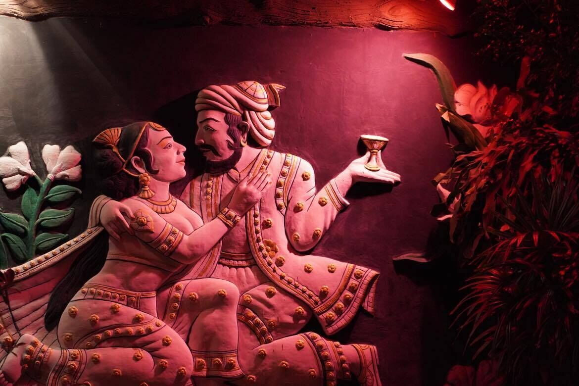Una estatua de un hombre y una mujer vestidos con atuendo tradicional, sentados en un banco con una taza entre ellos.